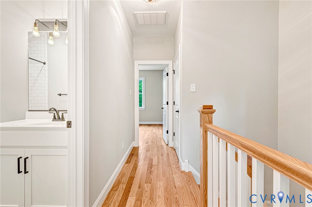 Hardwood flooring, white wall paint, white bathroom vanity with dark hardware, white subway tile shower surround, and a natural wood staircase handrail
