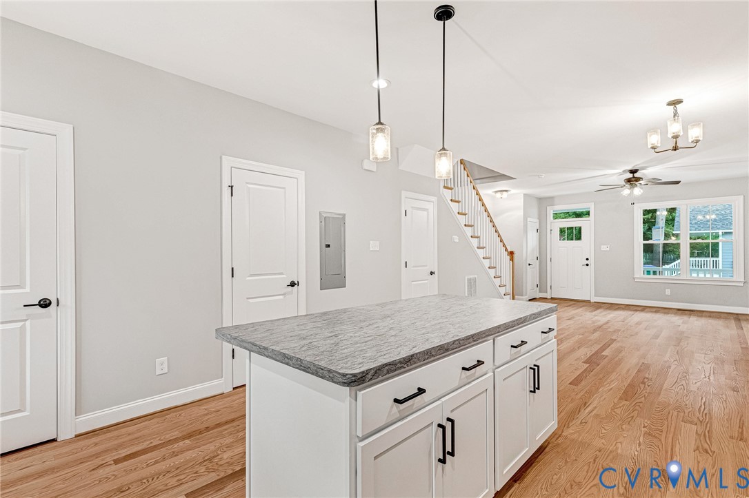 Kitchen island with stone-finish countertop, pendant lighting, hardwood-finish flooring, staircase with wood handrail, and white paneled doors