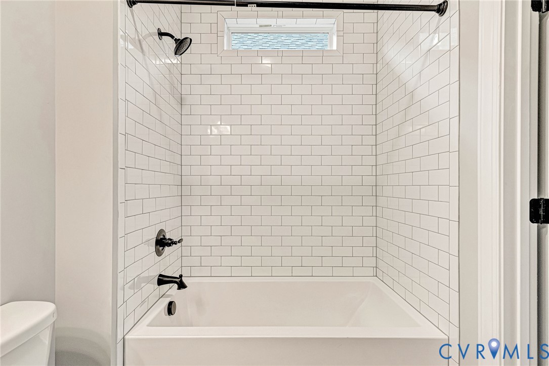Bathtub with white subway tile surround, matte black fixtures, and an upper transom window