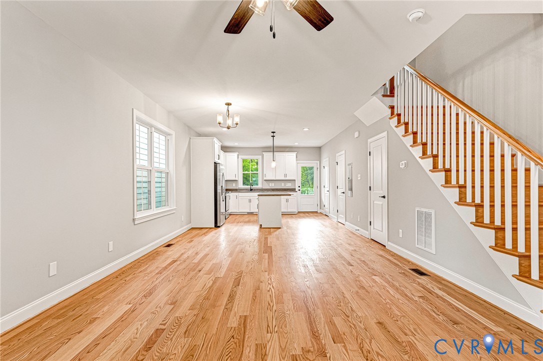 Hardwood flooring, white shaker cabinetry, stainless steel appliances, central island, and a wooden staircase
