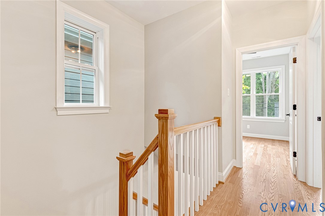 Bright hallway featuring gleaming wood-finish flooring, white painted walls, and a classic wooden staircase with white spindle railing