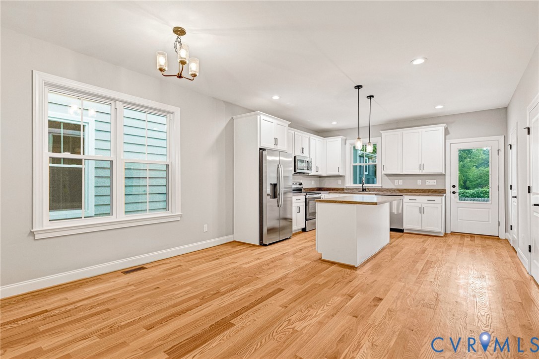 Hardwood flooring throughout, white shaker-style cabinetry, stainless steel appliances, kitchen island with pendant lighting, and recessed lighting