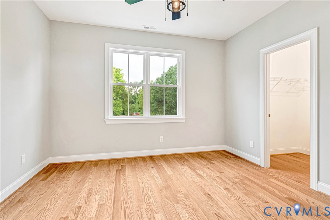 Hardwood flooring, white trim, window with natural lighting, ceiling light fixture, and closet with wire shelving