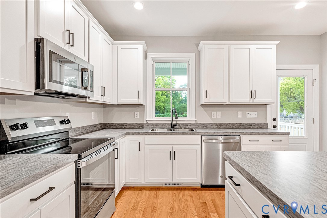 Kitchen featuring white cabinetry, light-toned countertops, stainless steel appliances, and wood-finish flooring