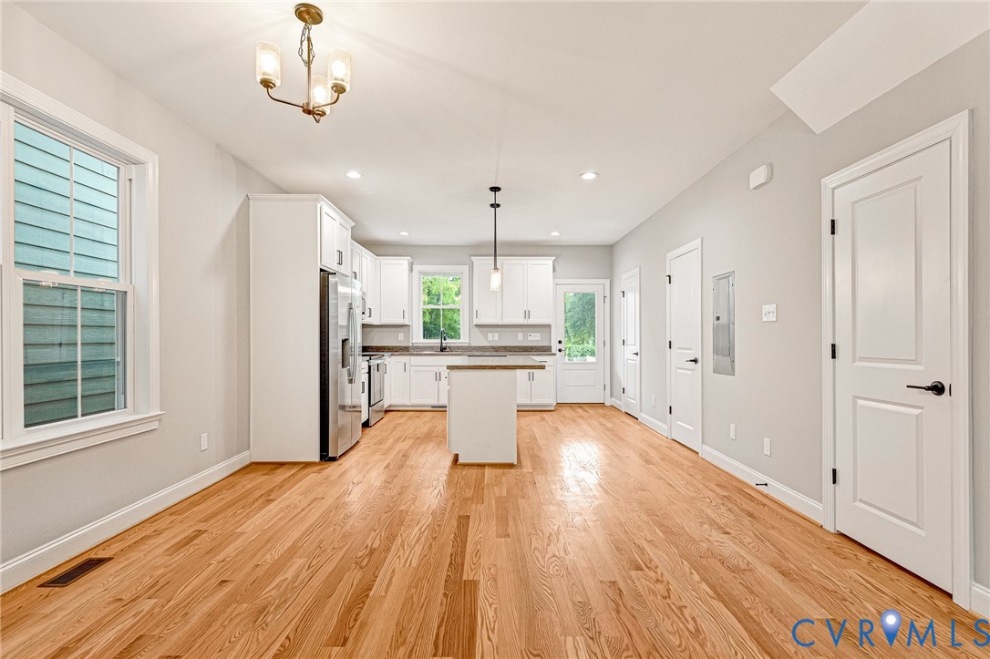 Open-concept living area featuring wood-finish flooring, white shaker cabinetry, stainless steel appliances, and recessed lighting