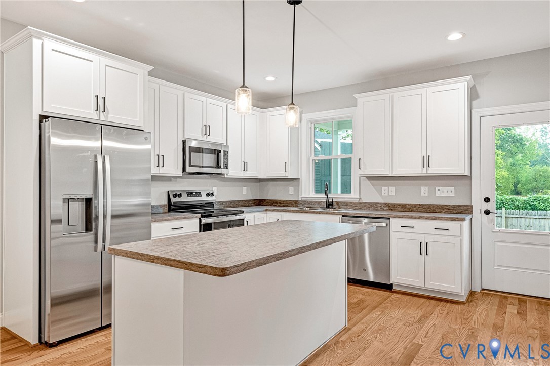 Kitchen featuring white shaker cabinetry, stainless steel appliances, a center island, pendant lighting, and wood-finish flooring