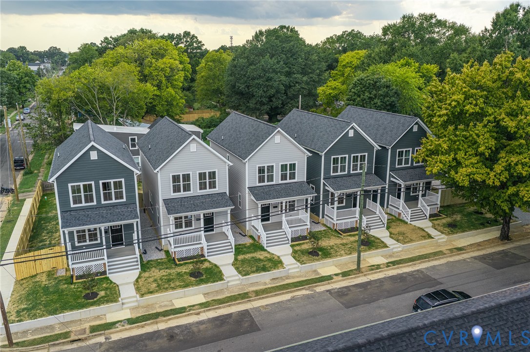 Newly constructed homes featuring a combination of light and dark siding, gabled roofs, front porches with white railings, and paved sidewalks