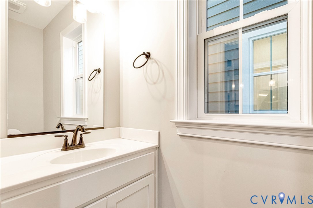 White vanity with cabinet storage, integrated sink, bronze-finish faucet, and coordinating towel ring