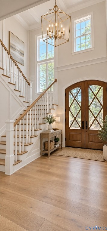 Hardwood flooring, wood-paneled staircase with white balusters, arched double entry doors with diamond-patterned glass, transom windows, and a coffered ceiling