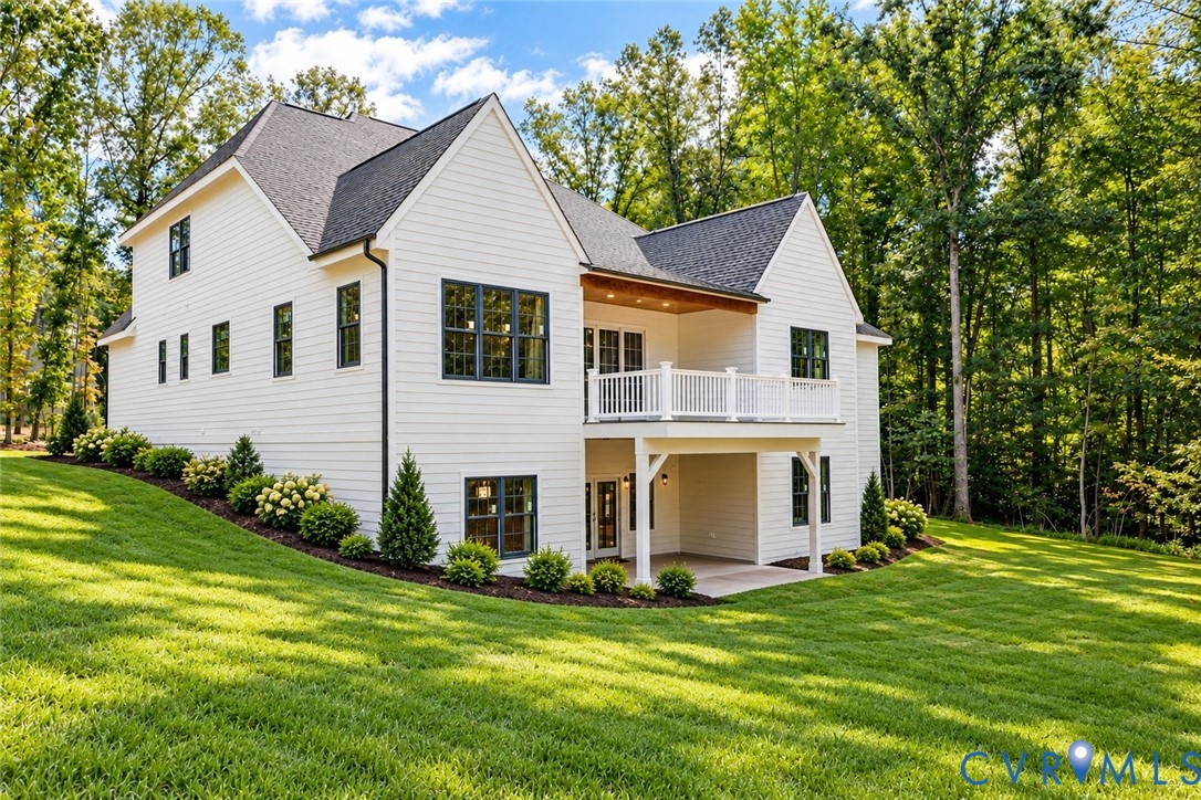 White siding exterior with dark-framed windows, a second-story balcony with white railings, and a covered ground-level patio