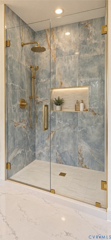 Glass-enclosed shower with blue-toned veined wall tile, brass-finish fixtures, a built-in recessed shelf with backlighting, and a tiled shower pan