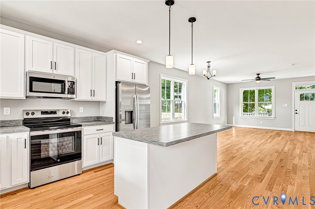 Open-concept living space with wood-finish flooring, white cabinetry, stainless steel appliances, and a kitchen island with a stone countertop