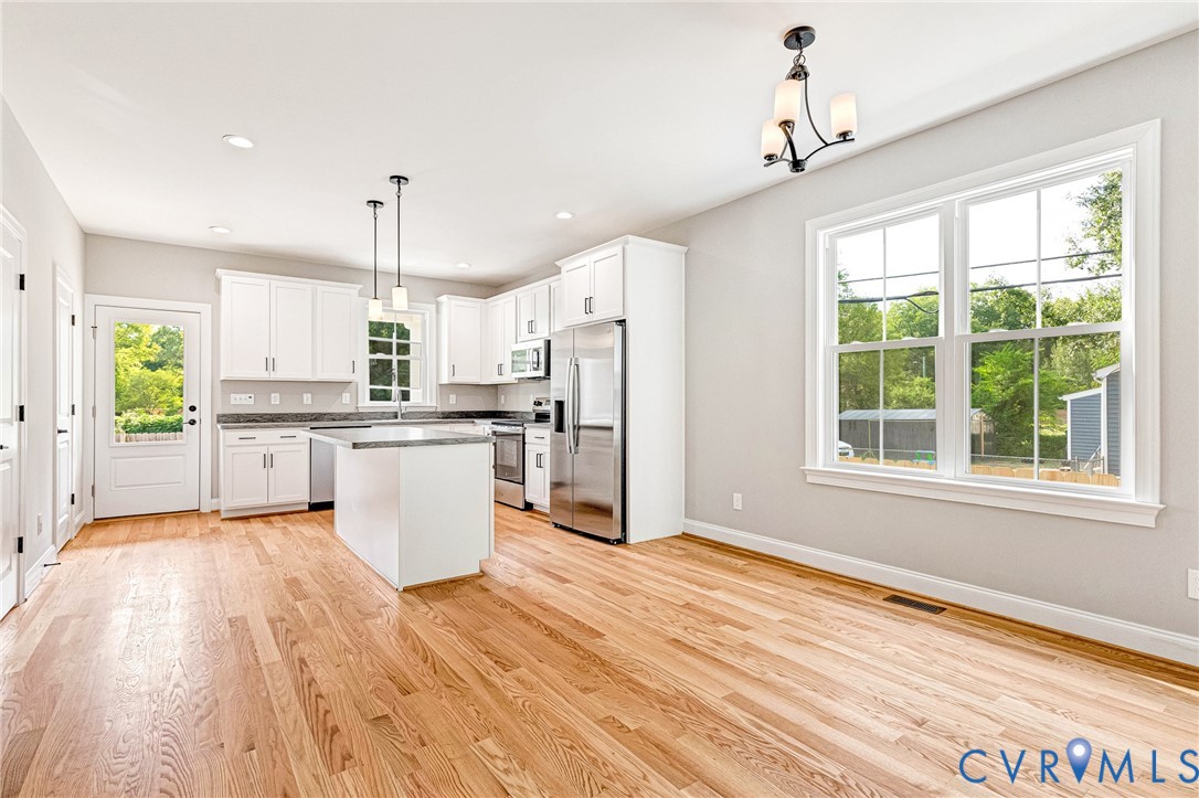 Open-concept interior featuring light wood flooring, white cabinetry, stainless steel appliances, a kitchen island with pendant lighting, and recessed ceiling lights