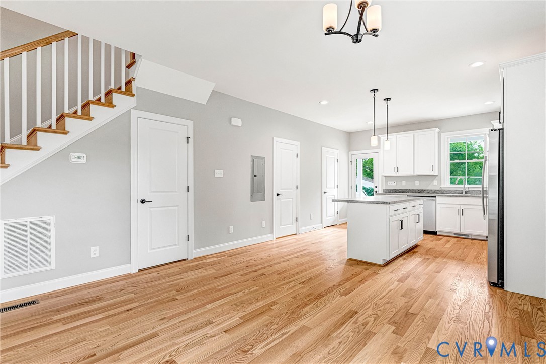 Hardwood flooring throughout, white shaker kitchen cabinetry, kitchen island with seating, stainless steel appliances, and a staircase with white balusters