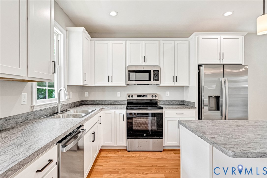 Kitchen featuring white cabinetry, stainless steel appliances, grey stone-finish countertops, a double basin sink, and wood-finish flooring