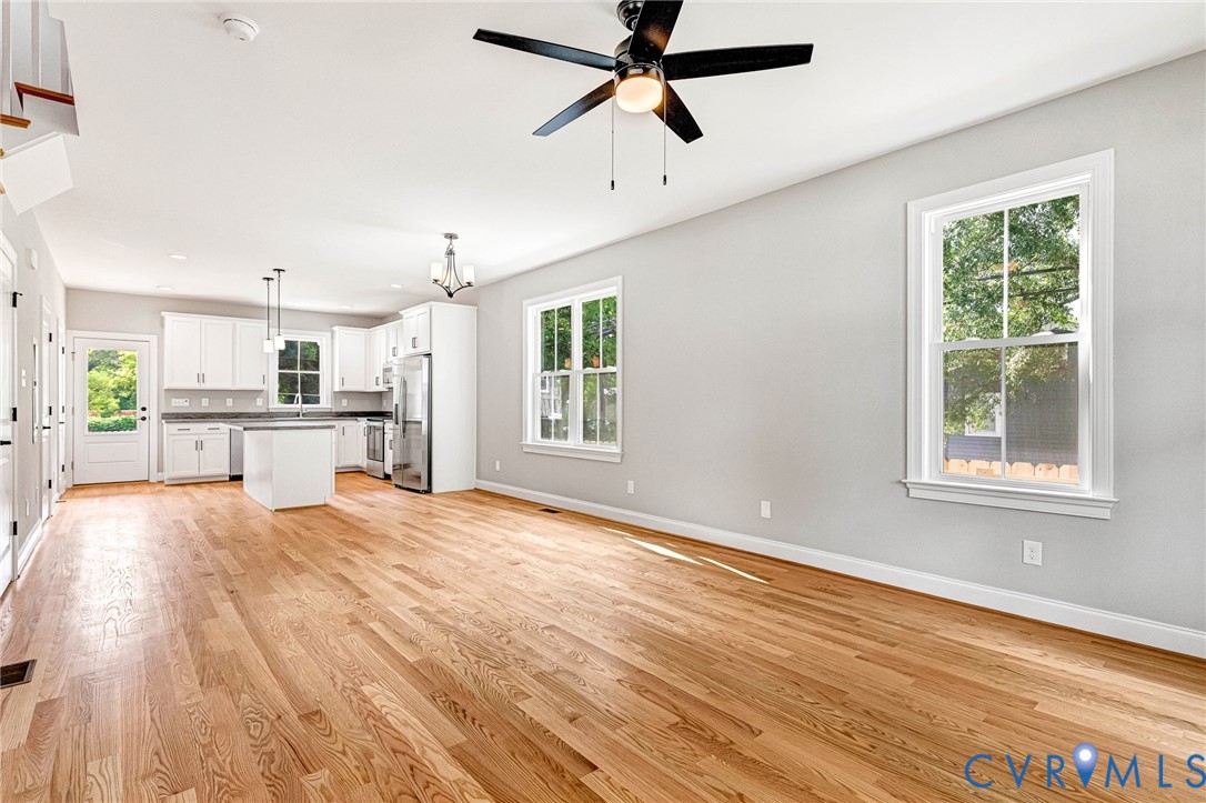 Hardwood flooring throughout, white kitchen cabinetry, stainless steel appliances, kitchen island, and ceiling fan with integrated lighting Hardwood flooring throughout, white kitchen cabinetry, stainless steel appliances, kitchen island, and ceiling fan with integrated lighting