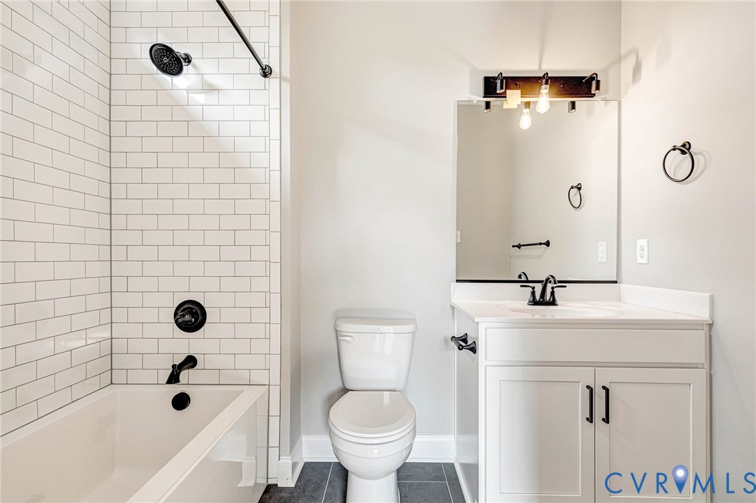 White subway tile shower surround with matte black fixtures, a white vanity with shaker-style cabinetry, and a countertop with an integrated sink