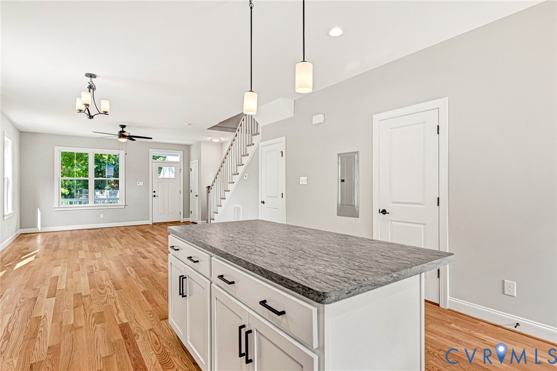 Wood-finish flooring, white shaker cabinetry, gray stone countertop, and two pendant lights