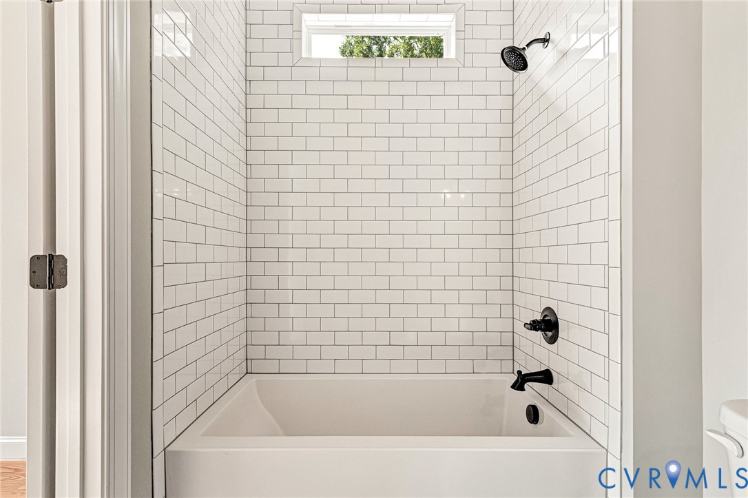 Bathtub with white subway tile surround, dark-finished shower head, and dark-finished tub fixtures