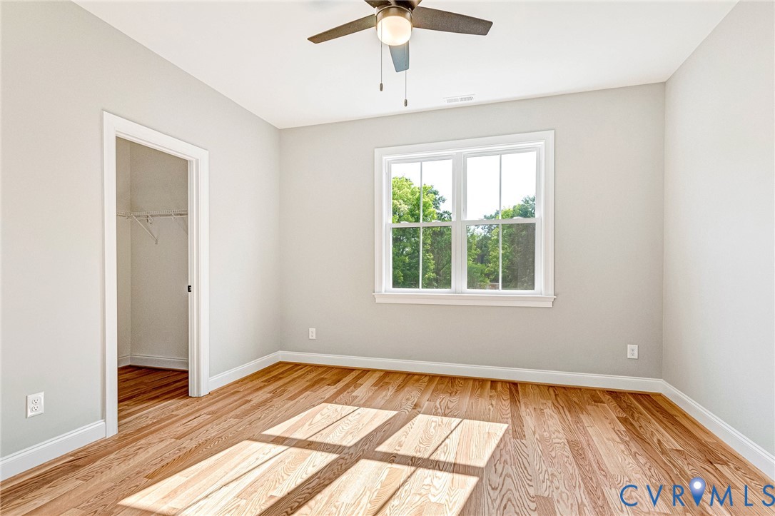 Hardwood flooring, white trim, recessed closet, ceiling fan, and a large window