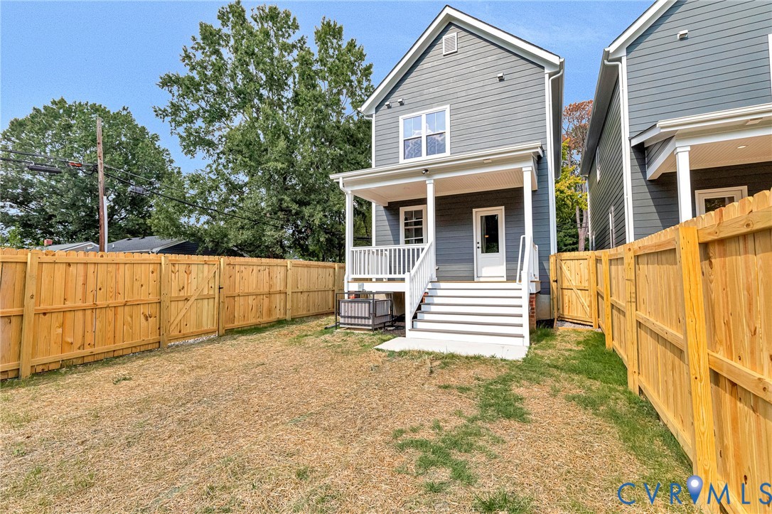 Rear exterior with gray siding, a covered porch with white columns, and a private wooden fence