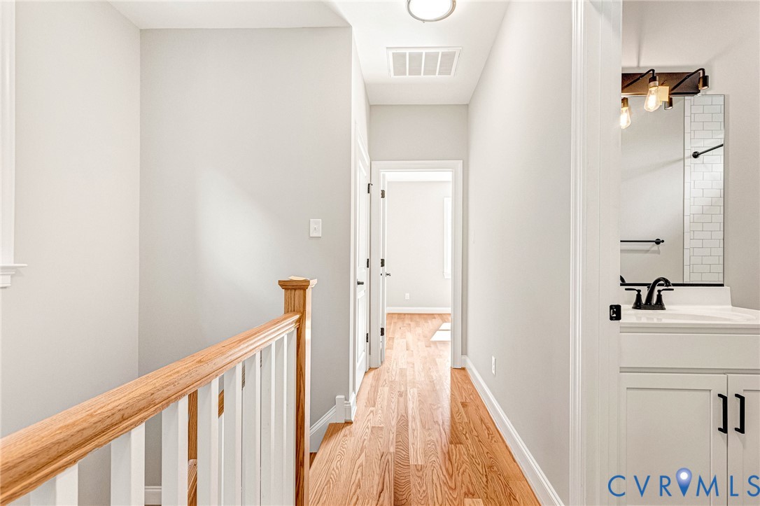 Hardwood flooring, painted white railing with natural wood-finish top, recessed lighting, white vanity with stone-finish countertop, matte black faucet, and subway tile backsplash