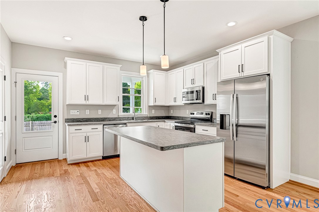 Kitchen featuring wood-finish flooring, white cabinetry, a central island, stainless steel appliances, and granite countertops