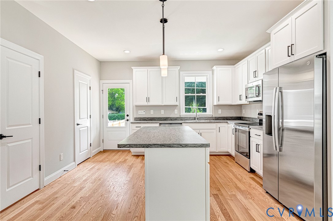 Kitchen featuring white cabinetry, stainless steel appliances, a center island with a stone countertop, and wood-finish flooring