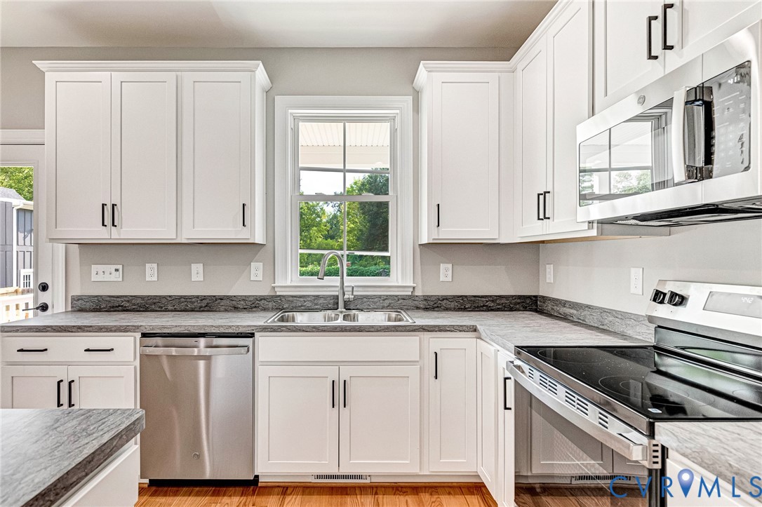 White shaker-style cabinetry with black hardware, stainless steel appliances, dark stone-finish countertops, and wood-finish flooring