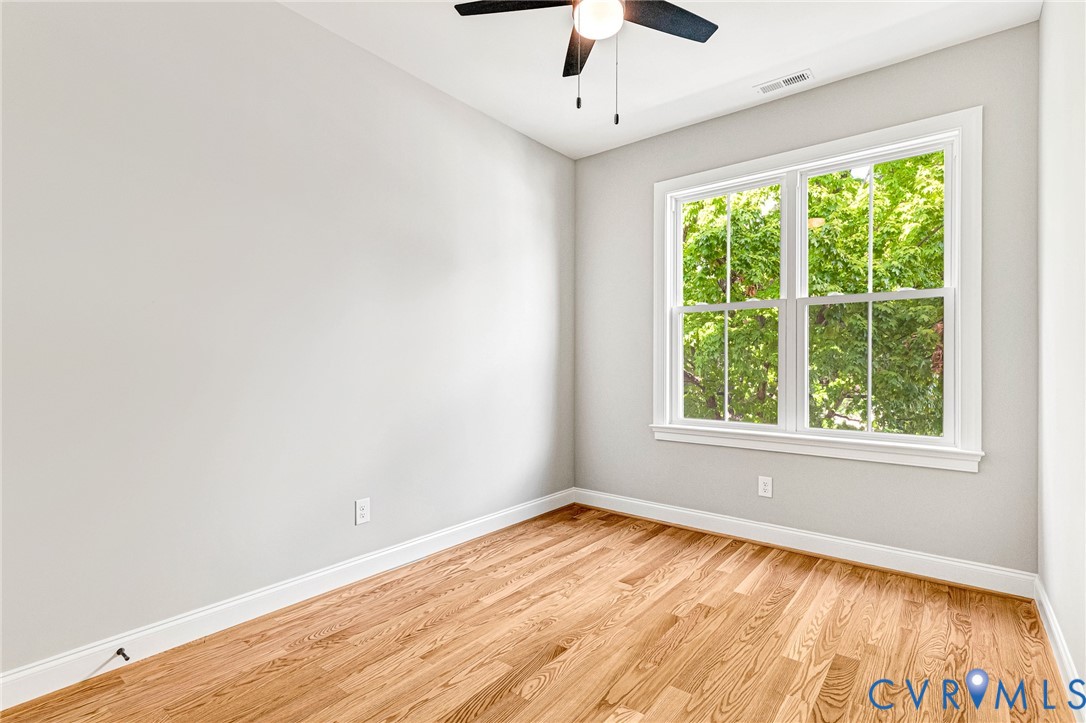 Hardwood flooring, painted walls, white trim, double-hung window, and a ceiling fan with integrated lighting