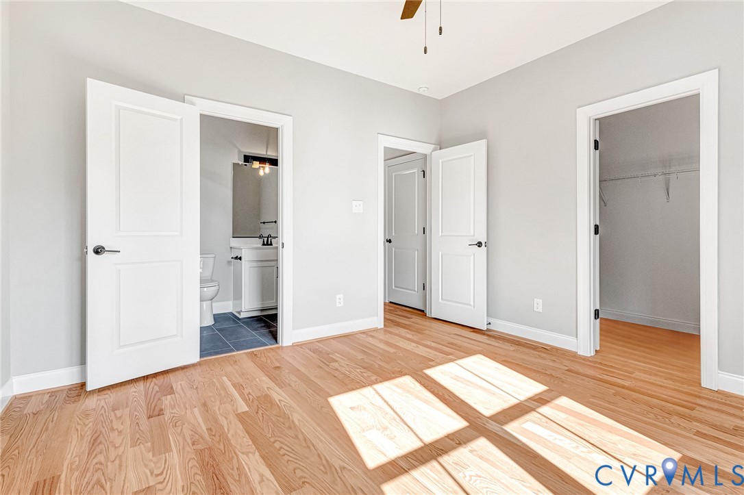 Hardwood flooring, light gray wall finishes, white trim, ceiling fan, and access to a full bathroom