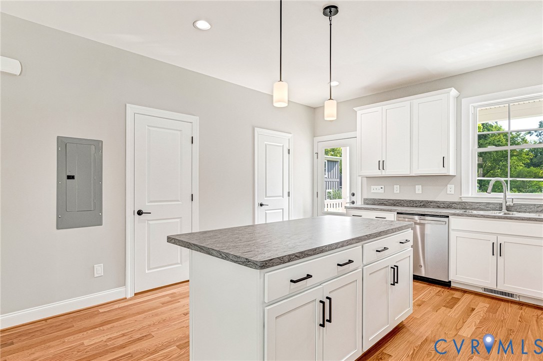 White cabinetry with black hardware, a center island featuring a gray countertop, stainless steel dishwasher, and wood-finish flooring