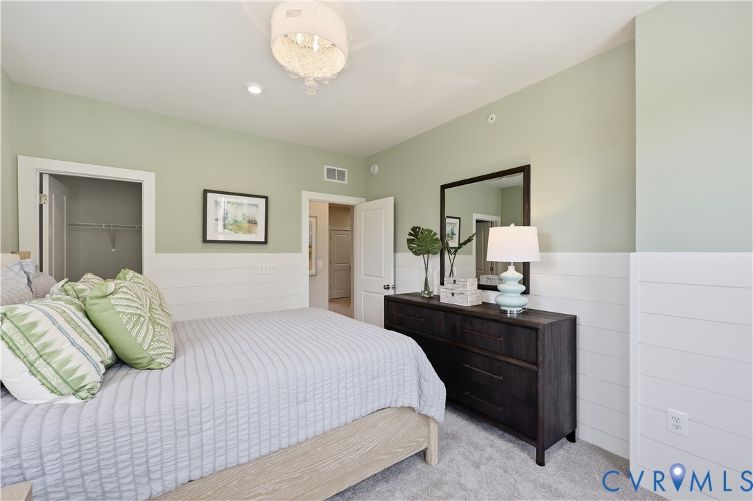 Bedroom featuring light green walls with white shiplap wainscoting, a carpeted floor, and a decorative ceiling light fixture Bedroom featuring light green walls with white shiplap wainscoting, a carpeted floor, and a decorative ceiling light fixture