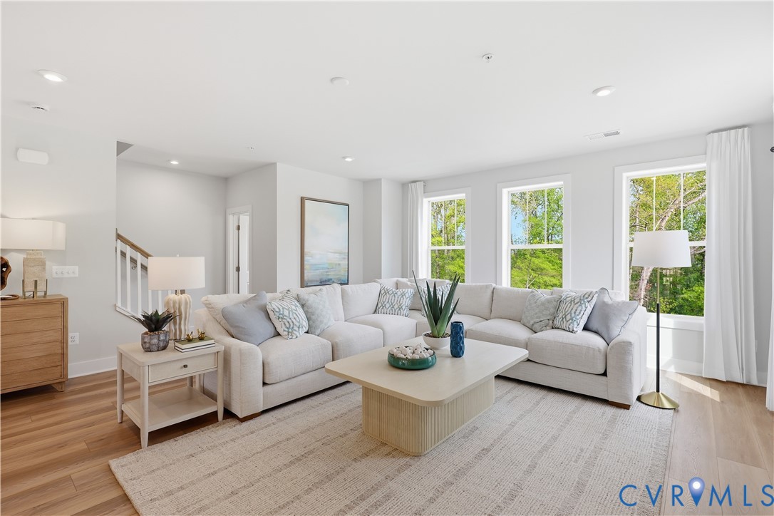 Spacious living area featuring light wood-finish flooring, recessed lighting, and multiple large windows