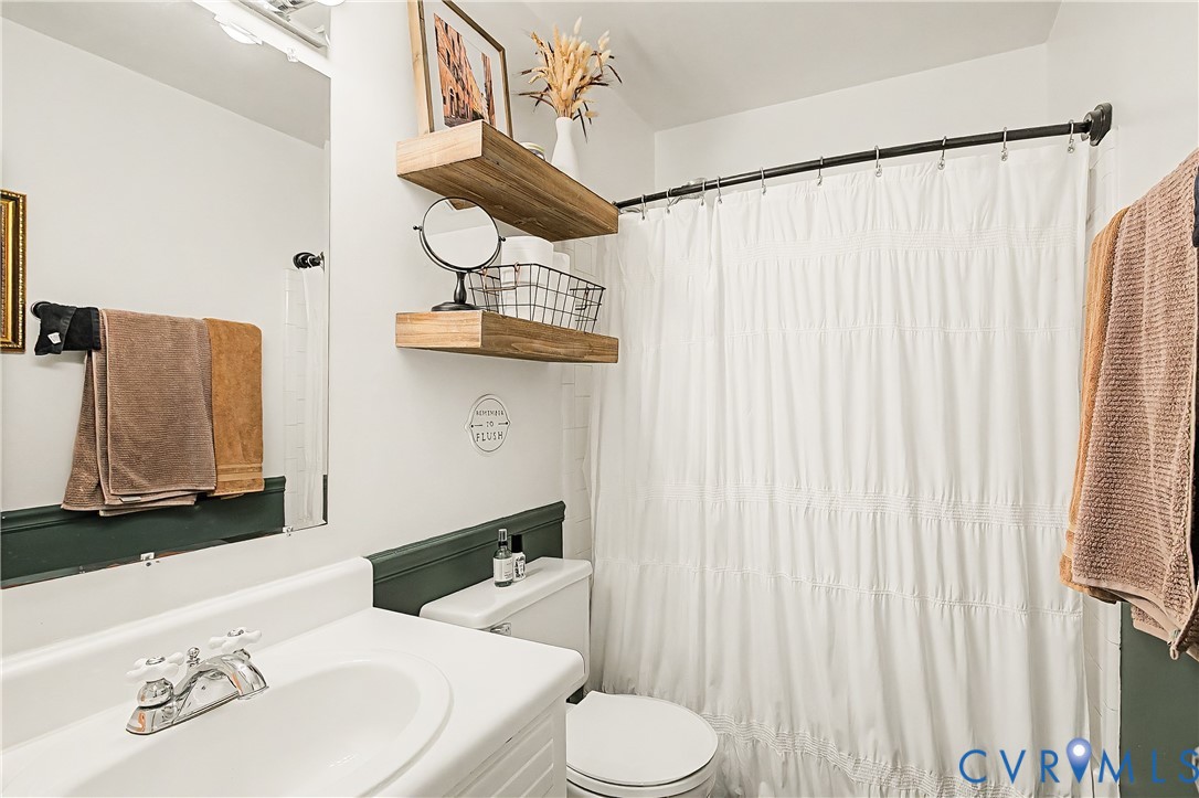 Bathroom with wood-finish floating shelves, a white vanity with integrated sink, and a white toilet
