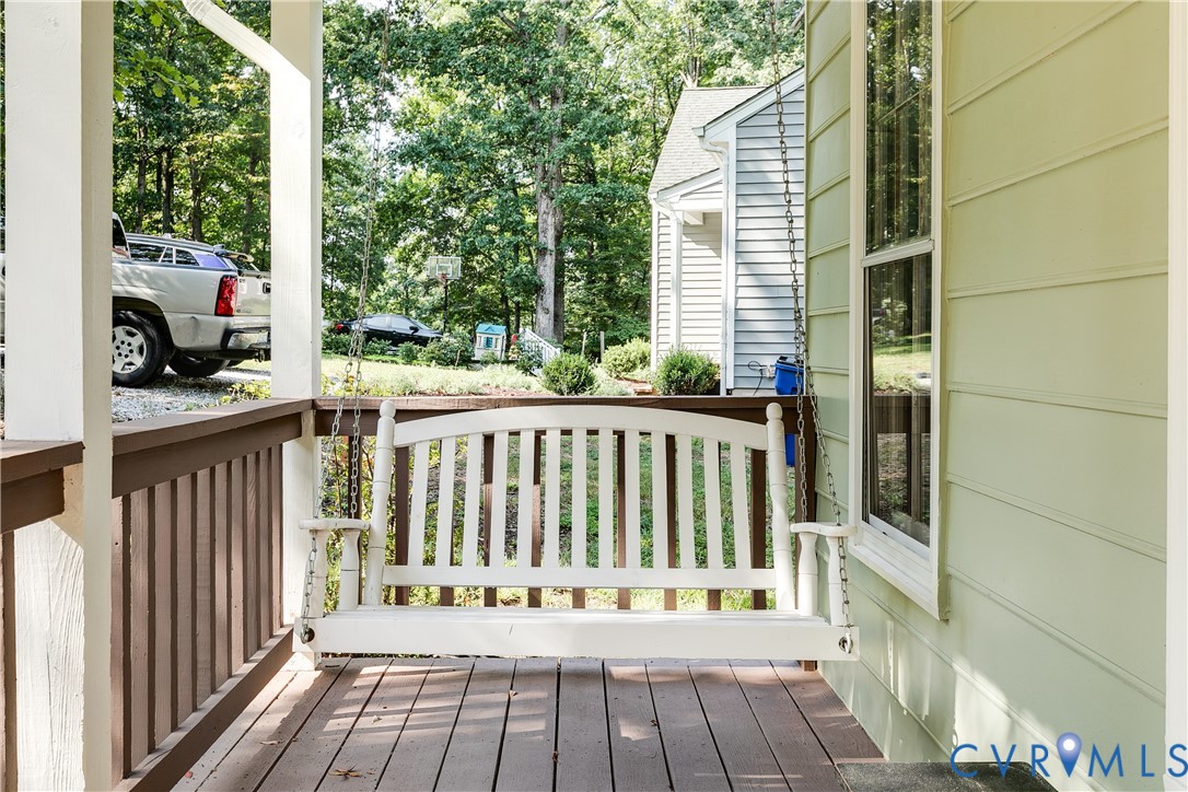 Covered porch featuring a white porch swing, wood-finish flooring, and a railing with vertical balusters