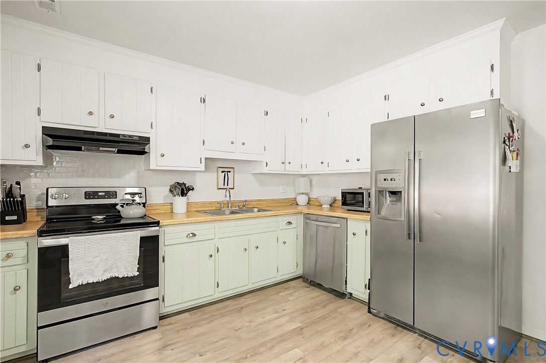 Kitchen featuring wood-finish flooring, two-tone cabinetry, wood countertops, a subway tile backsplash, and stainless steel appliances