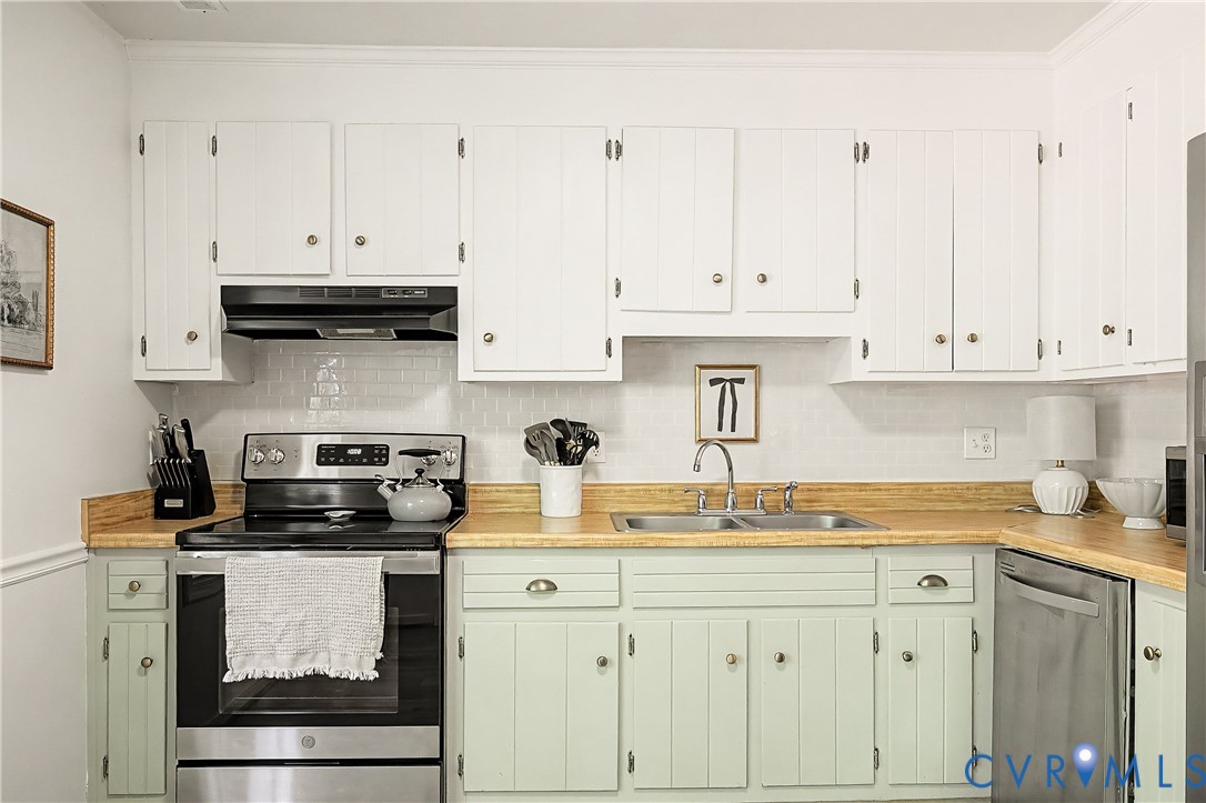 Kitchen featuring white upper cabinetry, light green lower cabinetry, wood-finish countertops, subway tile backsplash, and a stainless steel double basin sink