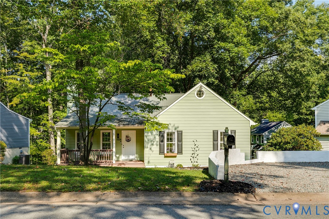 Mint green siding exterior with a front porch, a gravel driveway, and a mature tree canopy