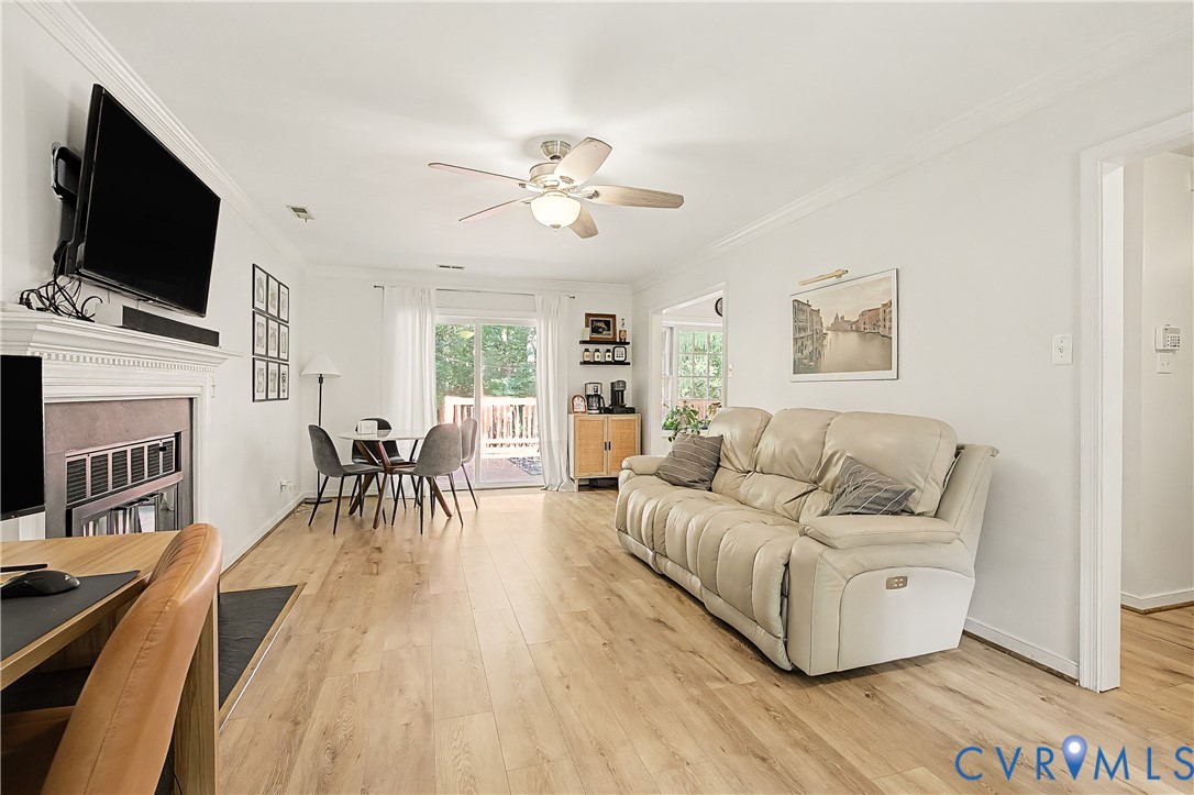 Light wood-finish flooring throughout, a white painted fireplace with a mantel, a glass sliding door, and a built-in ceiling fan with lighting