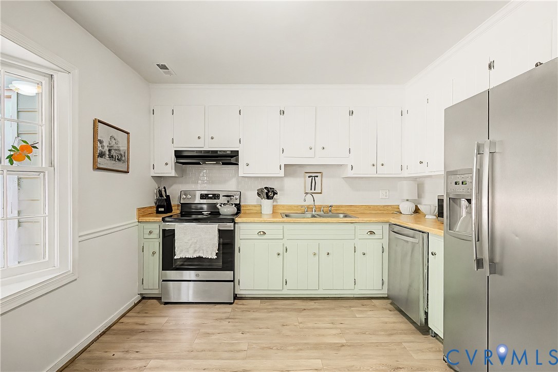 Kitchen featuring wood-finish flooring, white upper cabinetry, light-toned lower cabinetry, stainless steel appliances, and a window with white trim