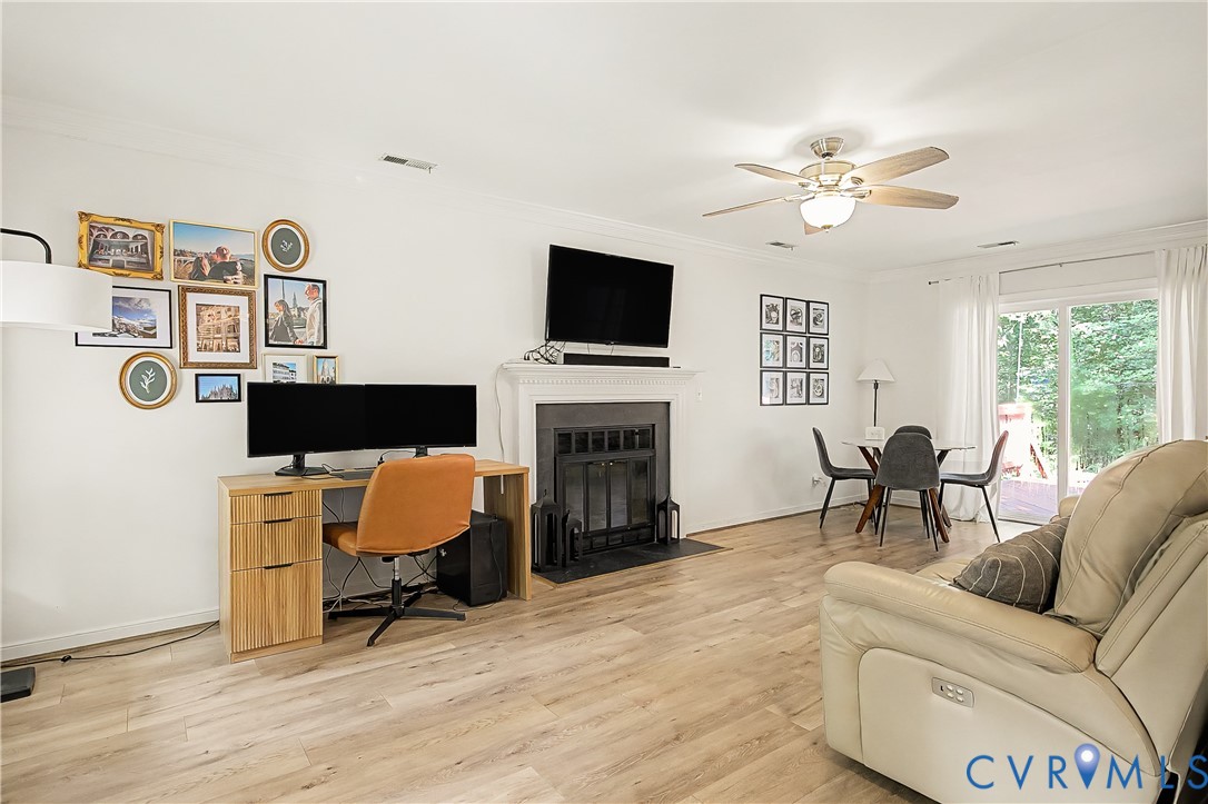 Wood-finish flooring throughout, fireplace with a black iron grate, white mantel, and ceiling fan with integrated lighting