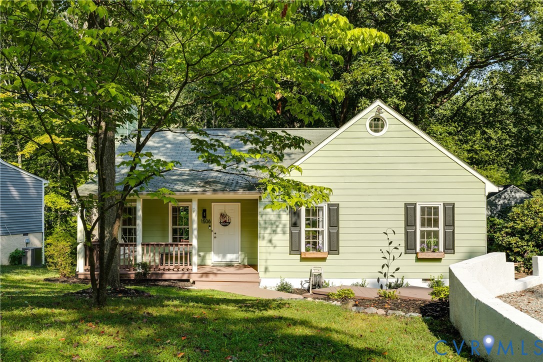 Gabled roofline with a round attic window, light green siding, dark window shutters, and a covered front porch with railings