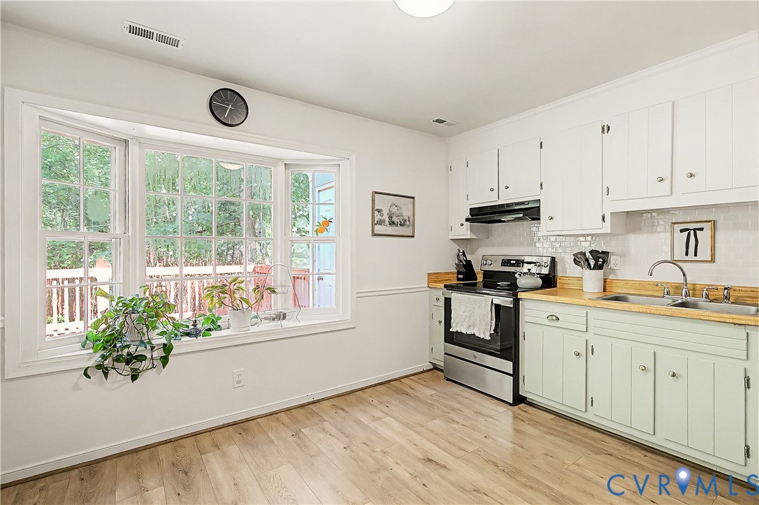 Wood-finish flooring, white upper cabinetry, stainless steel range, white tile backsplash, and a multi-pane bay window