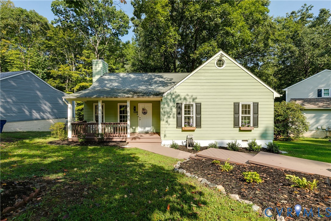 Light green siding exterior with a covered front porch, dark shutters, a circular attic window, and an established front garden bed