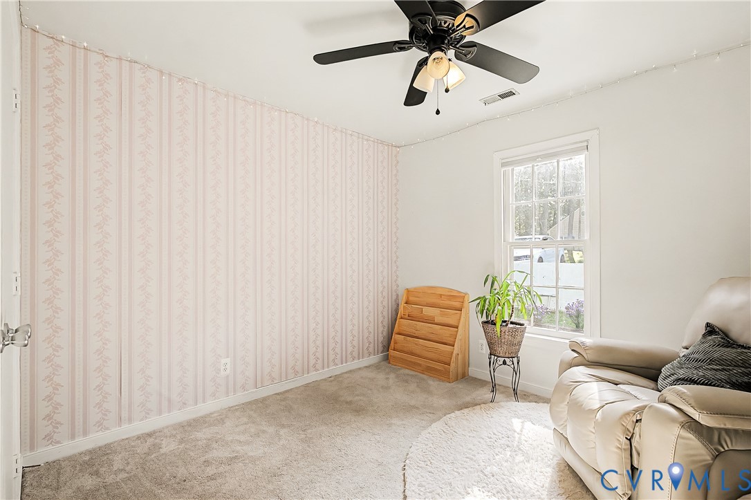 Carpeted room featuring a ceiling fan with integrated lighting, a double-hung window, and a wall with striped wallpaper