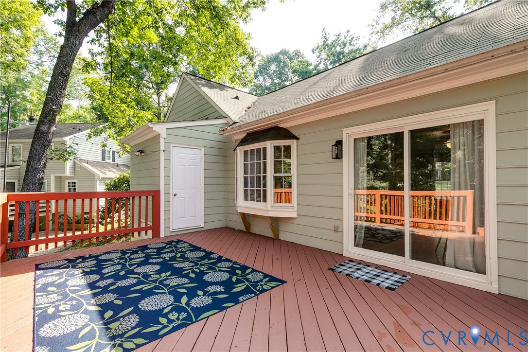 Expansive exterior deck with red wood railing, light green siding, a bay window, and a sliding glass door