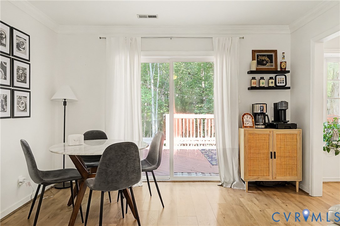 Light wood-finish flooring, white painted walls, crown molding, and a sliding glass door providing access to an exterior deck
