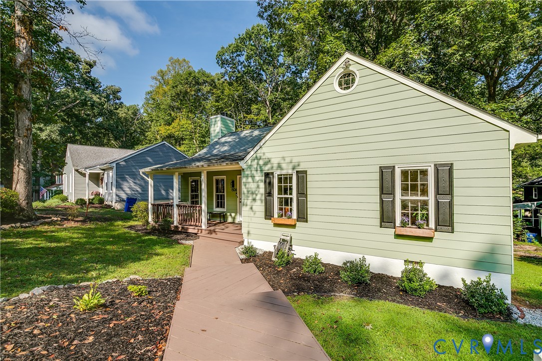 Light green siding with dark shutters, front porch with wood railings, and a front walkway