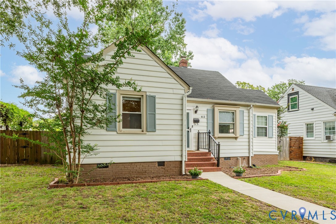White siding exterior with a dark-shingled roof, red brick foundation, and light blue window shutters